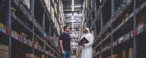 An Emirati and Western businessman meet in a busy Dubai warehouse, with a Crimson Legal booth prominent