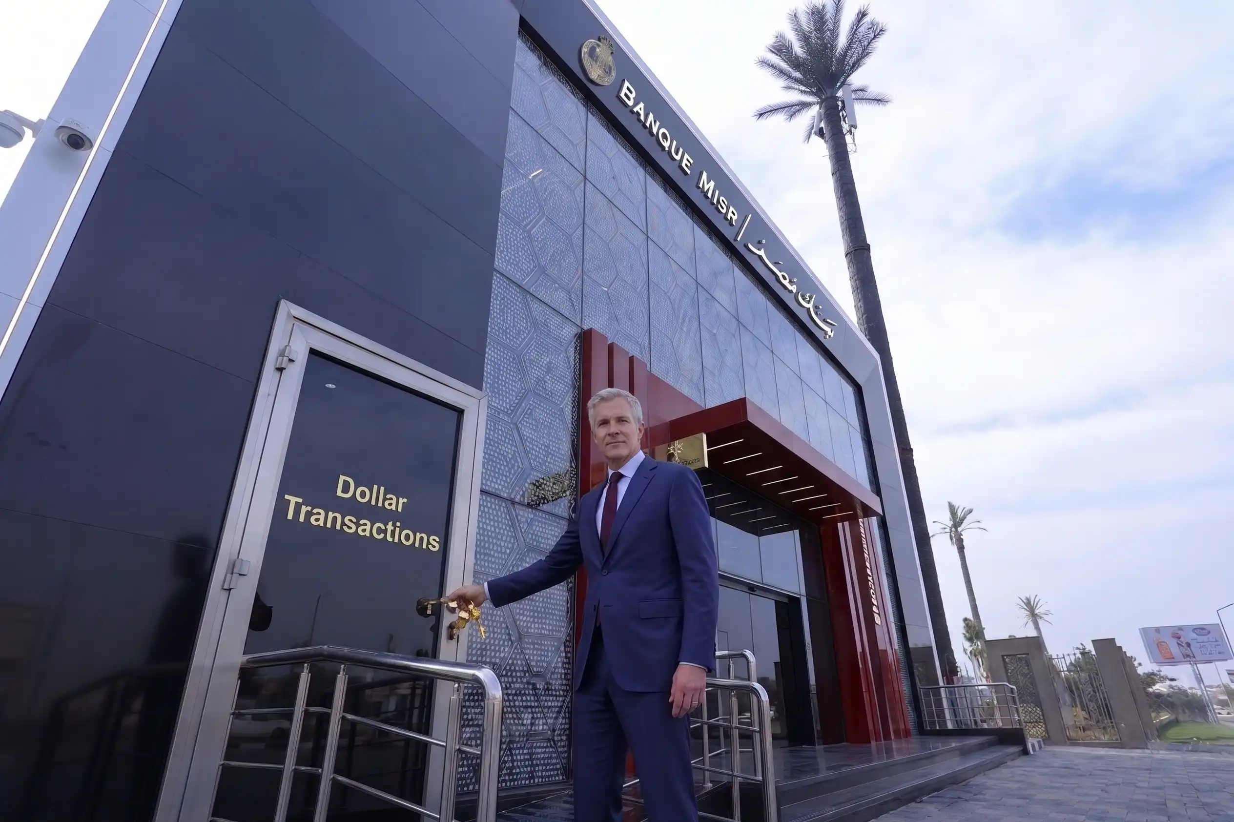A smartly dressed man in a blue suit stands outside the modern Banque Misr building near a dollar transactions door