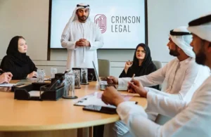 An Emirati man presents to professionals in traditional Gulf attire around a conference table before a Crimson Legal display screen.