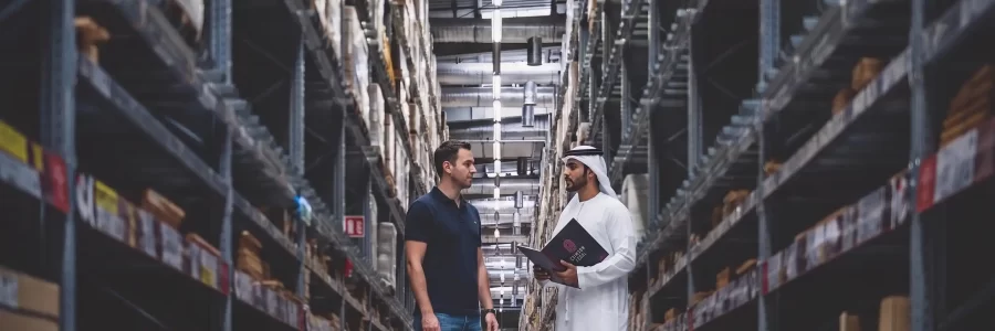 An Emirati and Western businessman meet in a busy Dubai warehouse, with a Crimson Legal booth prominent